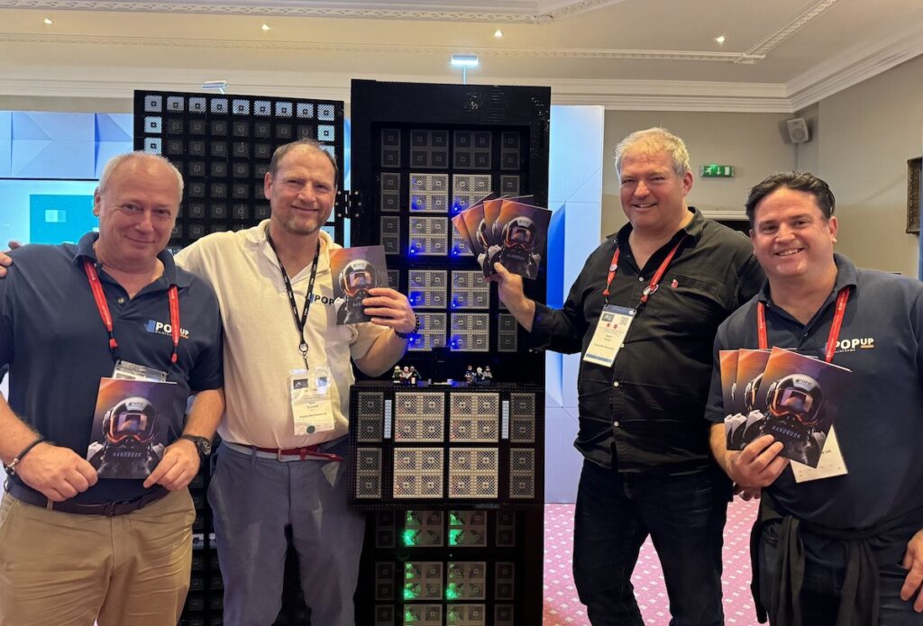 Four people standing in front of a lego z16 mainframe, smiling
